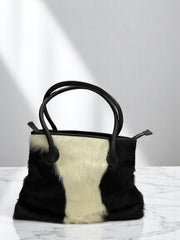 Black and white fur handbag on a marble surface with a white background